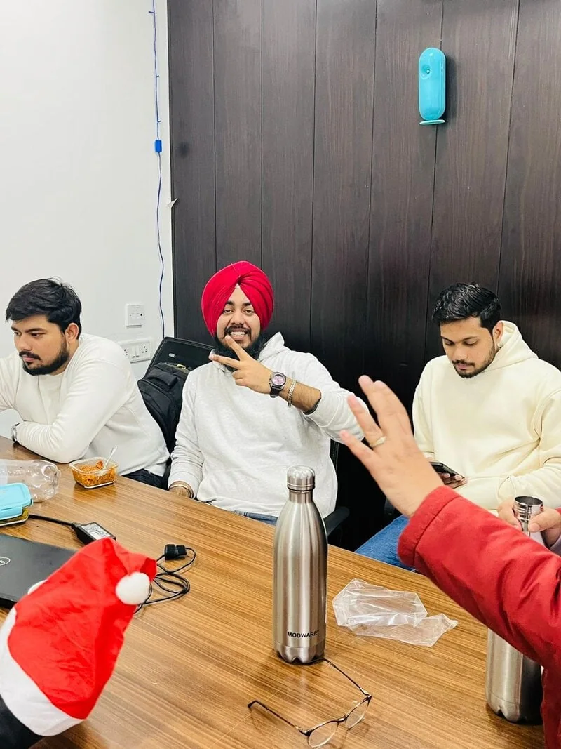 Three colleagues sitting at a table during the Christmas celebration, one making a peace sign.