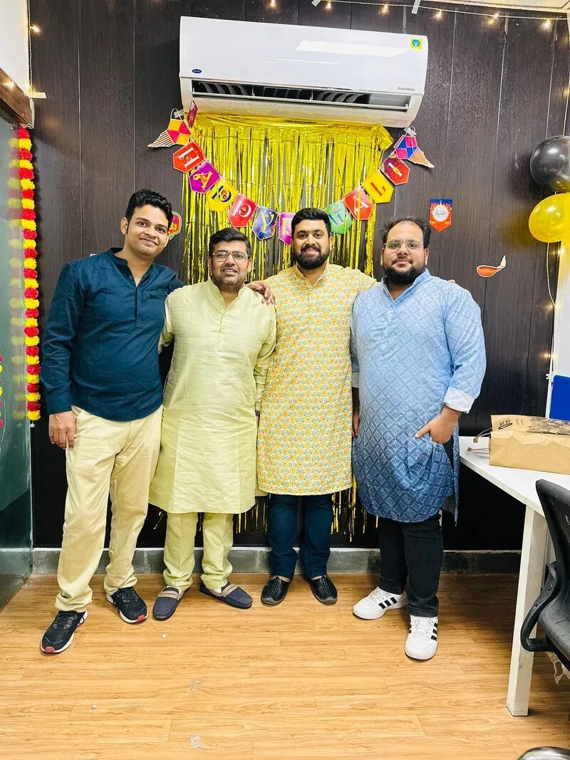 Four colleagues in kurtas posing together at a festive office party.