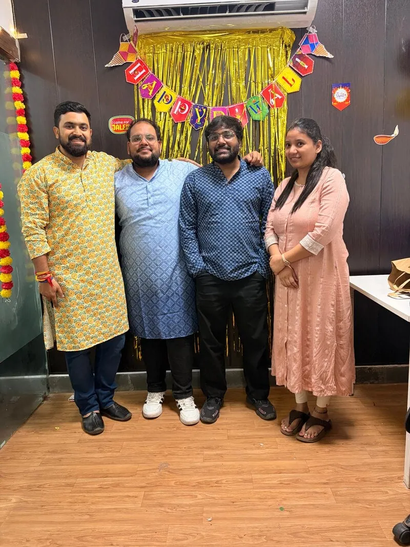 Four colleagues in traditional outfits posing together at the celebration.