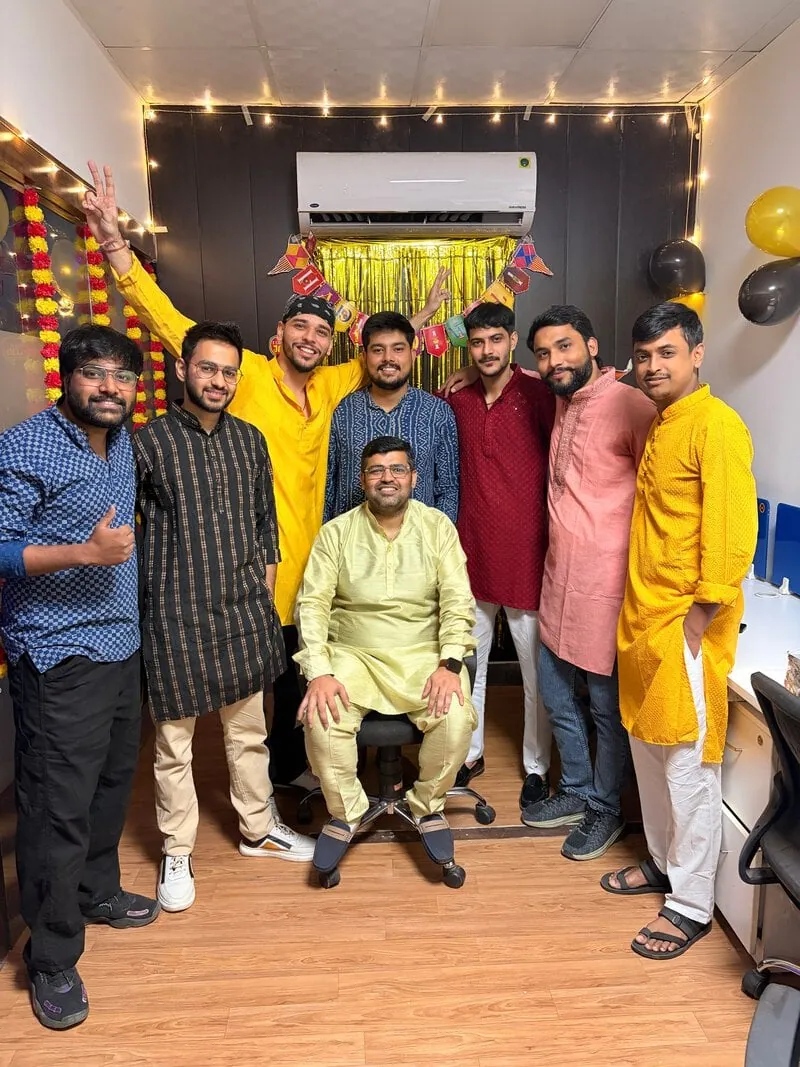 Group of colleagues in kurtas posing together, one seated, at the festival party.