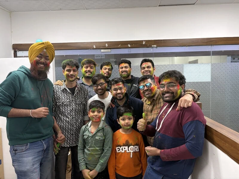 Group of colleagues posing together in the office, one wearing an orange turban and making a peace sign.