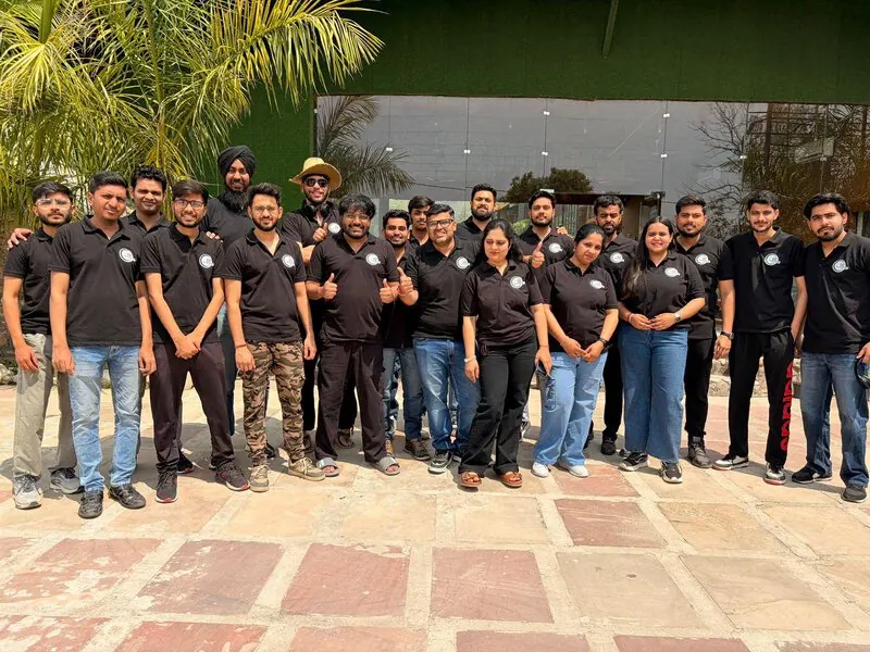 Team photo, black polos: Team group photo in matching black D2i shirts, posed outside a green-walled building entrance.