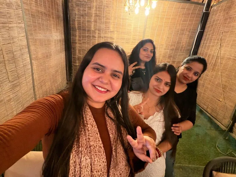 Four women selfie indoors: Four women taking a selfie indoors against a woven bamboo screen backdrop.