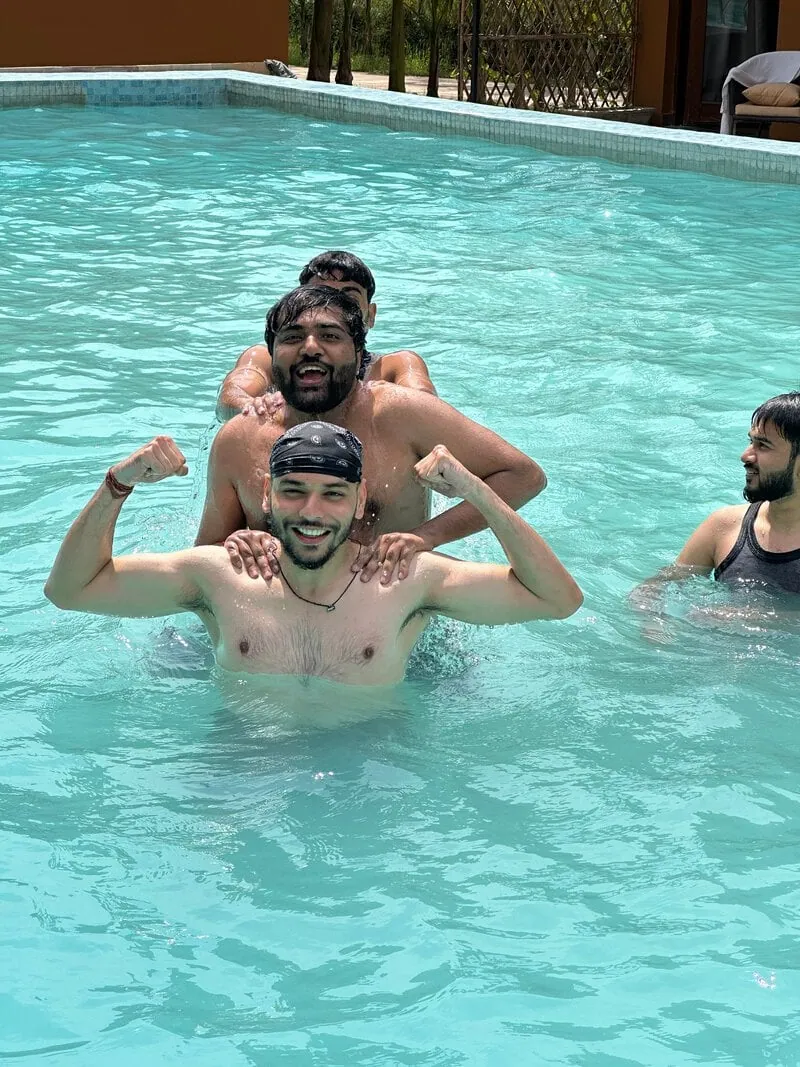 Pool, stacked shoulders: Three men in a swimming pool, stacked on each other's shoulders and flexing their arms.