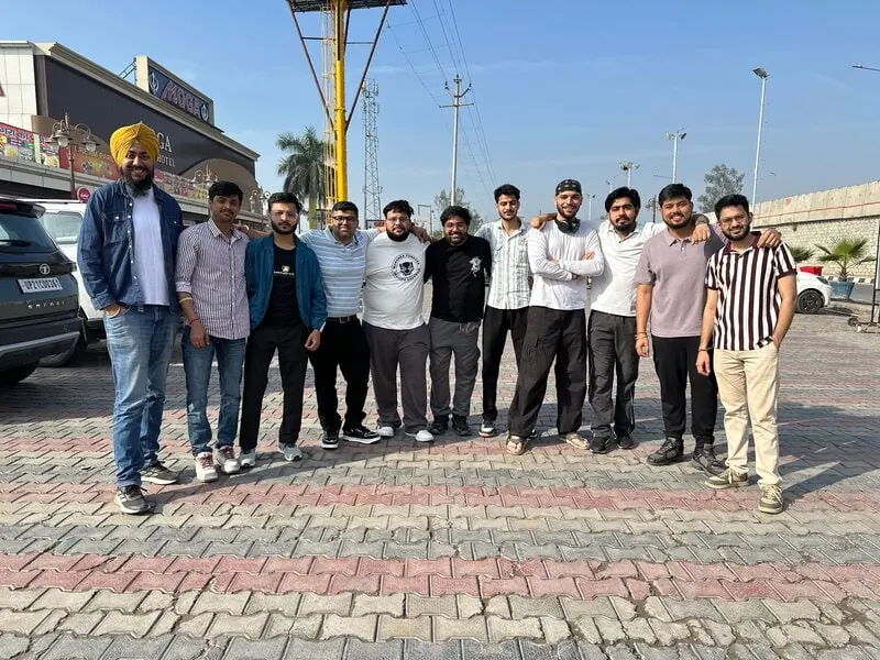 Group outside hotel: Eleven men standing in a row on a paved plaza, with a hotel signboard in the background.