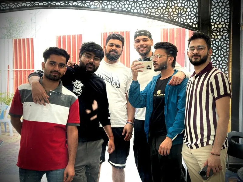 Six friends under archway: Six men posing together under a decorative lattice archway, one holding up a phone to take the photo.