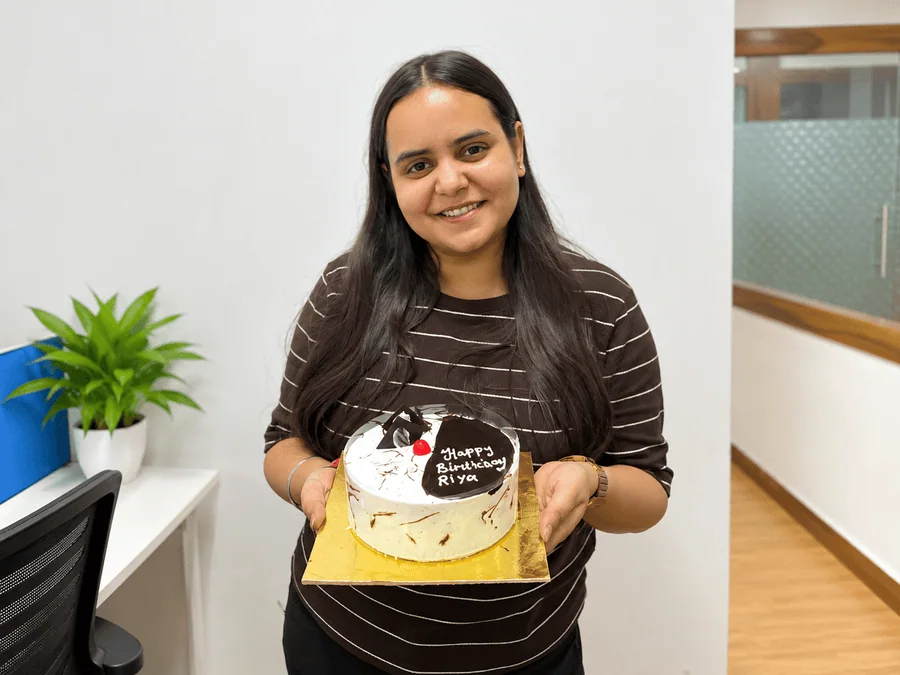 Riya Pandey smiling while holding a birthday cake during an office celebration.