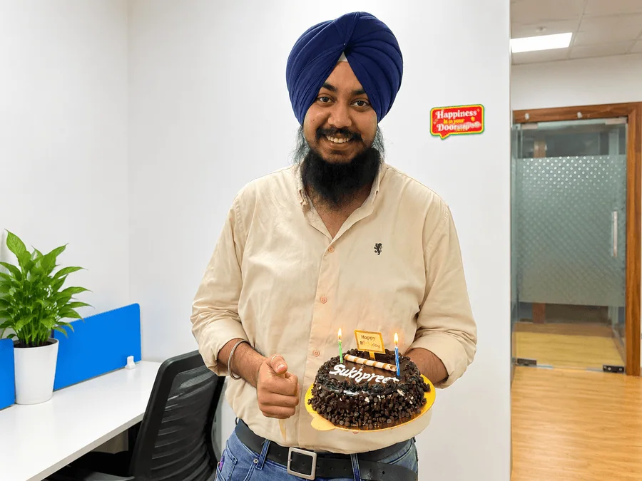 Sukhpreet Singh Sodhi holding a birthday cake during an office celebration.